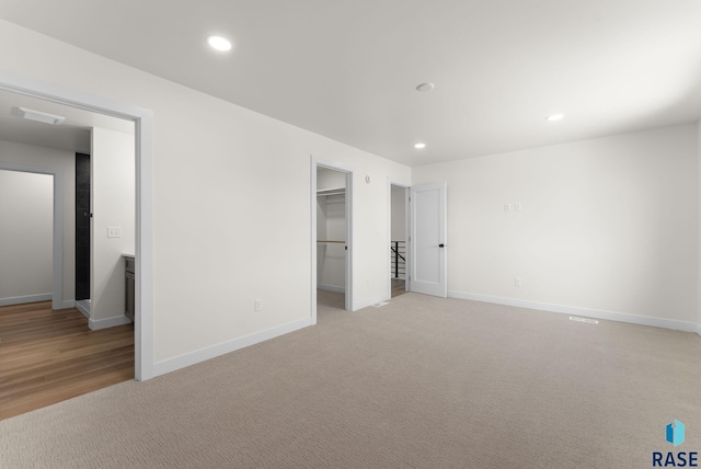 unfurnished bedroom featuring light carpet, a spacious closet, baseboards, and recessed lighting