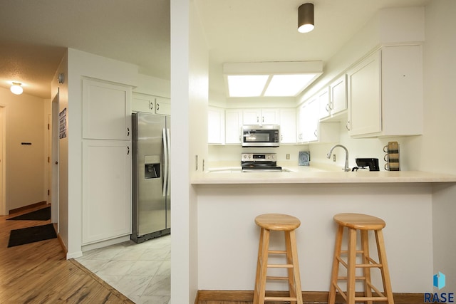 kitchen with stainless steel appliances, a breakfast bar, white cabinetry, and light countertops