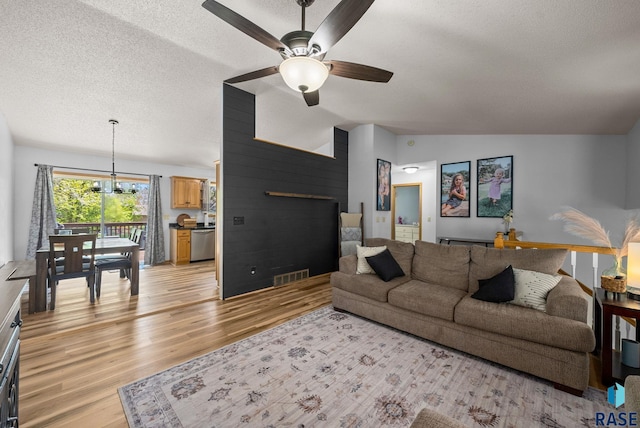 living room featuring a textured ceiling, light wood-style floors, ceiling fan, vaulted ceiling, and wooden walls