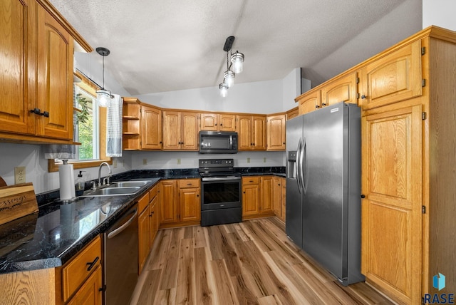 kitchen with appliances with stainless steel finishes, a sink, lofted ceiling, light wood-style floors, and a textured ceiling
