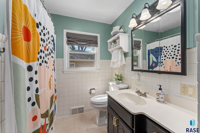 bathroom with tile patterned floors, vanity, tile walls, toilet, and wainscoting