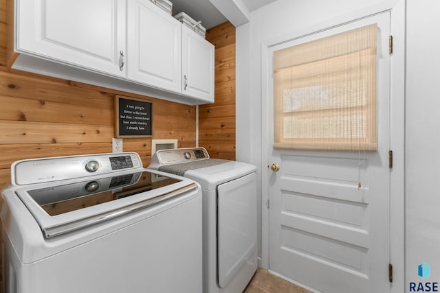 clothes washing area with washing machine and dryer, wood walls, cabinet space, and tile patterned flooring