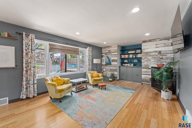 living room featuring a stone fireplace, wood finished floors, recessed lighting, baseboards, and built in features
