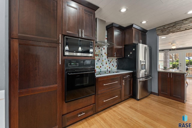 kitchen with black appliances, wall chimney exhaust hood, light wood-style flooring, light countertops, and dark brown cabinets