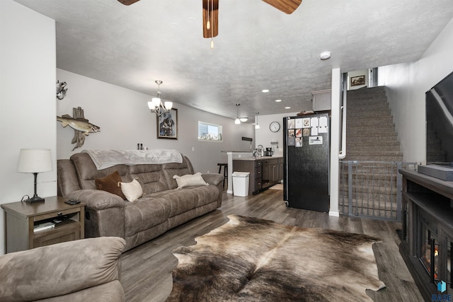 living area featuring a ceiling fan, wood finished floors, stairs, a textured ceiling, and a chandelier