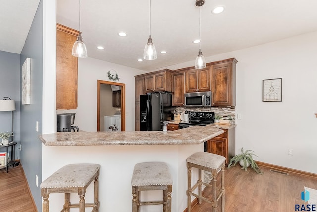 615 Marsha Cir, Tea, SD 57064 - kitchen with black appliances, washing machine and dryer, a breakfast bar area, light wood-type flooring, and recessed lighting