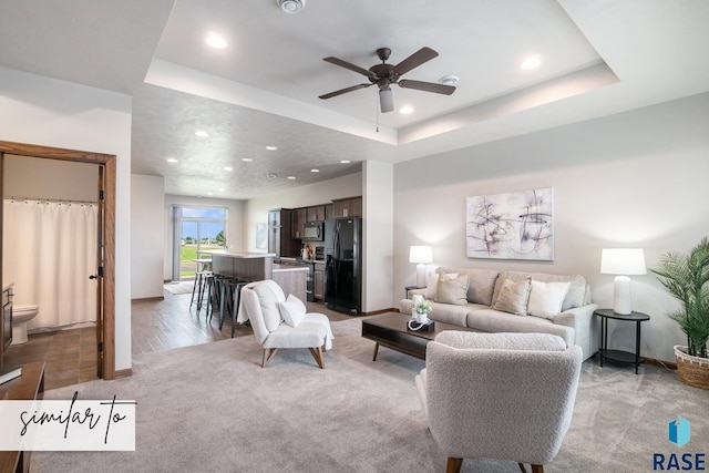 living area featuring light carpet, recessed lighting, ceiling fan, a raised ceiling, and baseboards