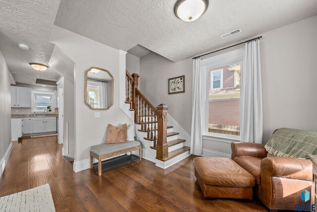 living area with a textured ceiling, wood finished floors, baseboards, and stairs