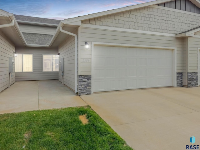 property exterior at dusk with stone siding, a garage, driveway, and board and batten siding