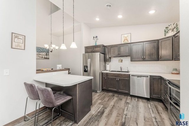 kitchen featuring appliances with stainless steel finishes, dark brown cabinetry, a breakfast bar, light wood-type flooring, and light countertops