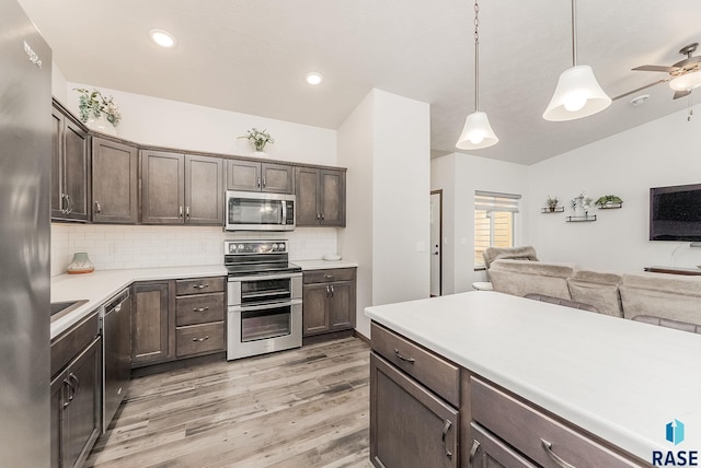 kitchen with appliances with stainless steel finishes, dark brown cabinets, open floor plan, light wood-type flooring, and recessed lighting
