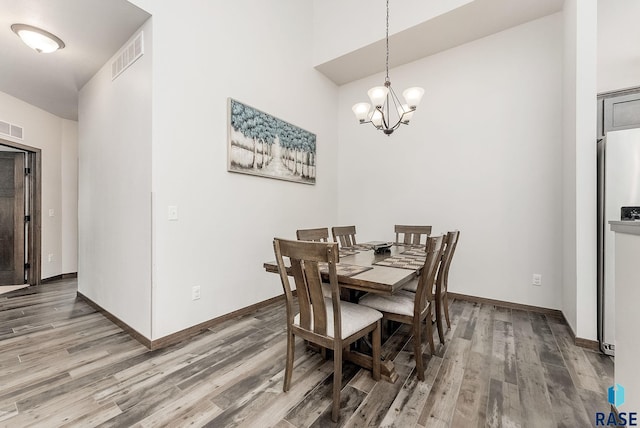 dining space with wood finished floors, a chandelier, baseboards, and a high ceiling