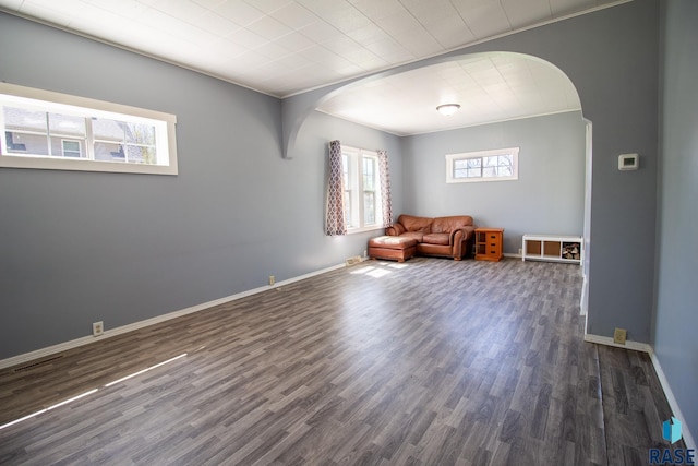 unfurnished room with arched walkways, healthy amount of natural light, wood finished floors, baseboards, and crown molding