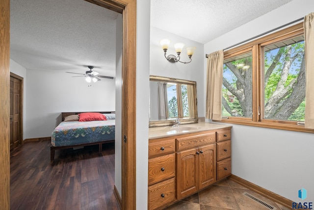 ensuite bathroom with a textured ceiling, healthy amount of natural light, baseboards, vanity, and ceiling fan