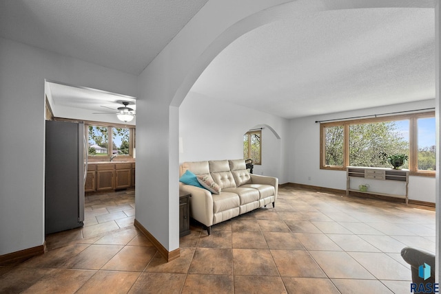 living area with arched walkways, healthy amount of natural light, baseboards, and a textured ceiling
