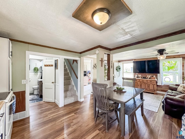 dining space featuring a textured ceiling, a ceiling fan, stairs, wood finished floors, and ornamental molding