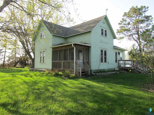 rear view of house with a sunroom, a lawn, a wooden deck, and a shingled roof