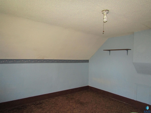 additional living space with vaulted ceiling, a textured ceiling, dark carpet, and baseboards