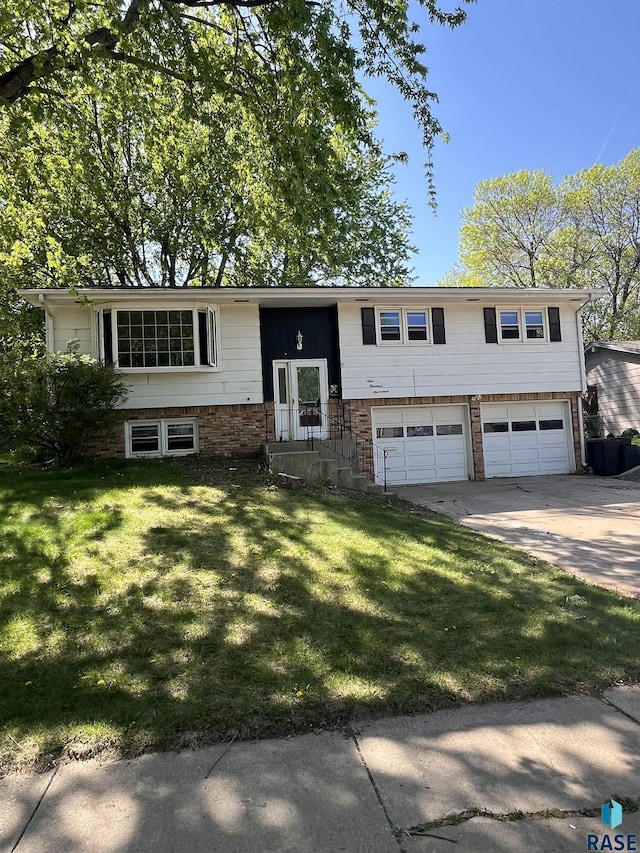 raised ranch featuring a garage, concrete driveway, and a front lawn