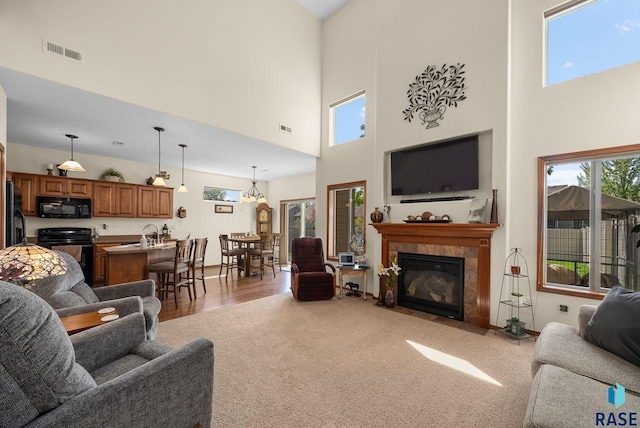 carpeted living room featuring a high ceiling, a tile fireplace, a sink, and wood finished floors