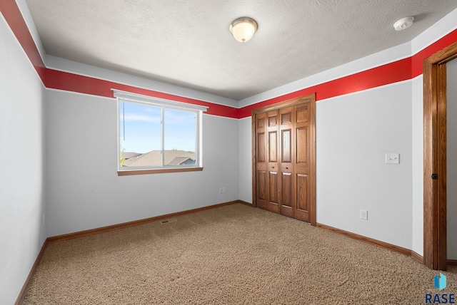 unfurnished bedroom featuring carpet flooring, a closet, baseboards, and a textured ceiling
