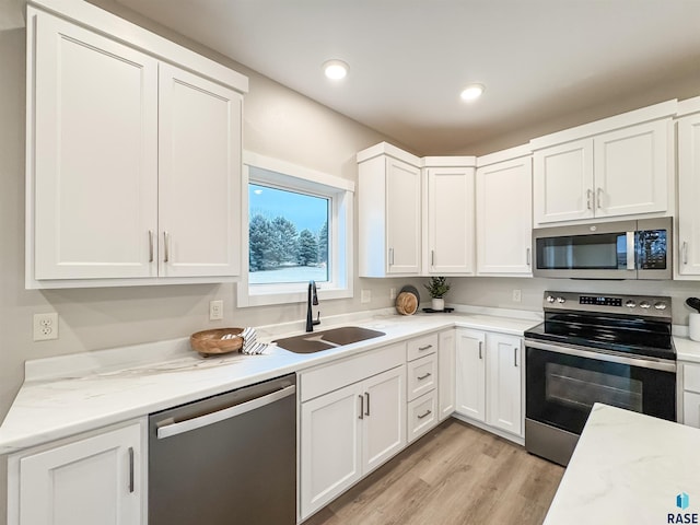 kitchen with stainless steel appliances, a sink, white cabinets, light wood finished floors, and recessed lighting