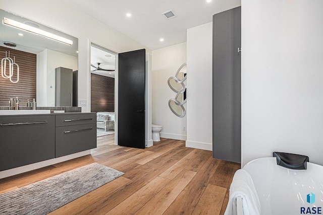 bathroom with hardwood / wood-style floors, toilet, vanity, recessed lighting, and a soaking tub