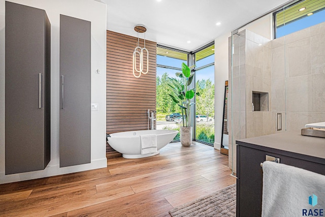 bathroom with a wall of windows, a freestanding tub, wood finished floors, and recessed lighting