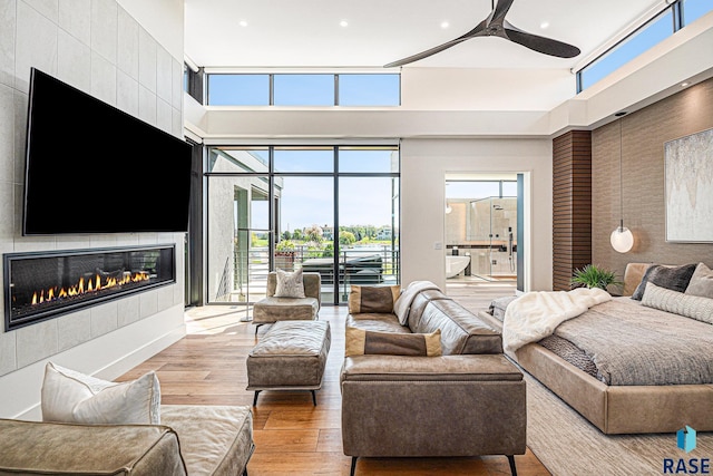 living area featuring a fireplace, a ceiling fan, wood finished floors, recessed lighting, and a high ceiling