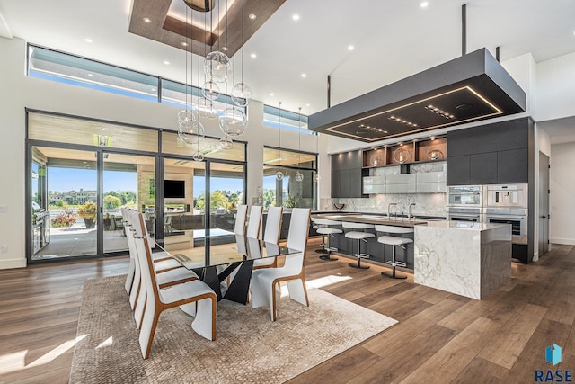 dining room featuring a towering ceiling, dark wood-style floors, a chandelier, recessed lighting, and baseboards