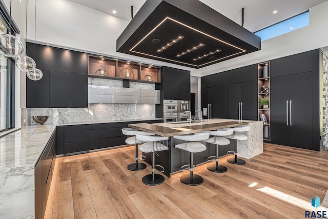 kitchen featuring open shelves, modern cabinets, dark cabinetry, backsplash, and a breakfast bar