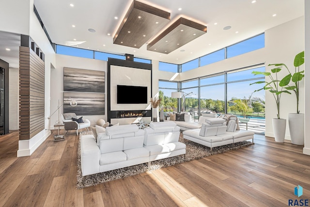 living area featuring a glass covered fireplace, recessed lighting, hardwood / wood-style flooring, and a high ceiling