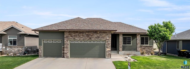 view of front facade featuring a garage, driveway, a front lawn, stone siding, and roof with shingles
