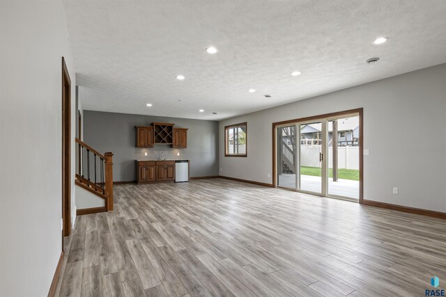 unfurnished living room featuring baseboards, recessed lighting, light wood finished floors, stairs, and a textured ceiling