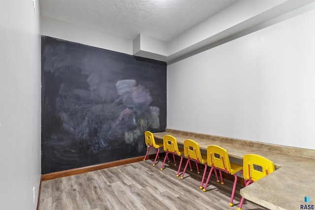 playroom with wood finished floors, a textured ceiling, and baseboards