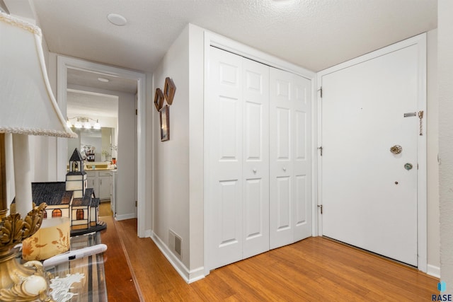 corridor with light wood-type flooring, a chandelier, baseboards, and a textured ceiling