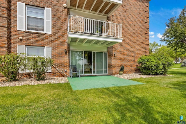 back of property featuring a balcony, brick siding, a patio area, and a yard