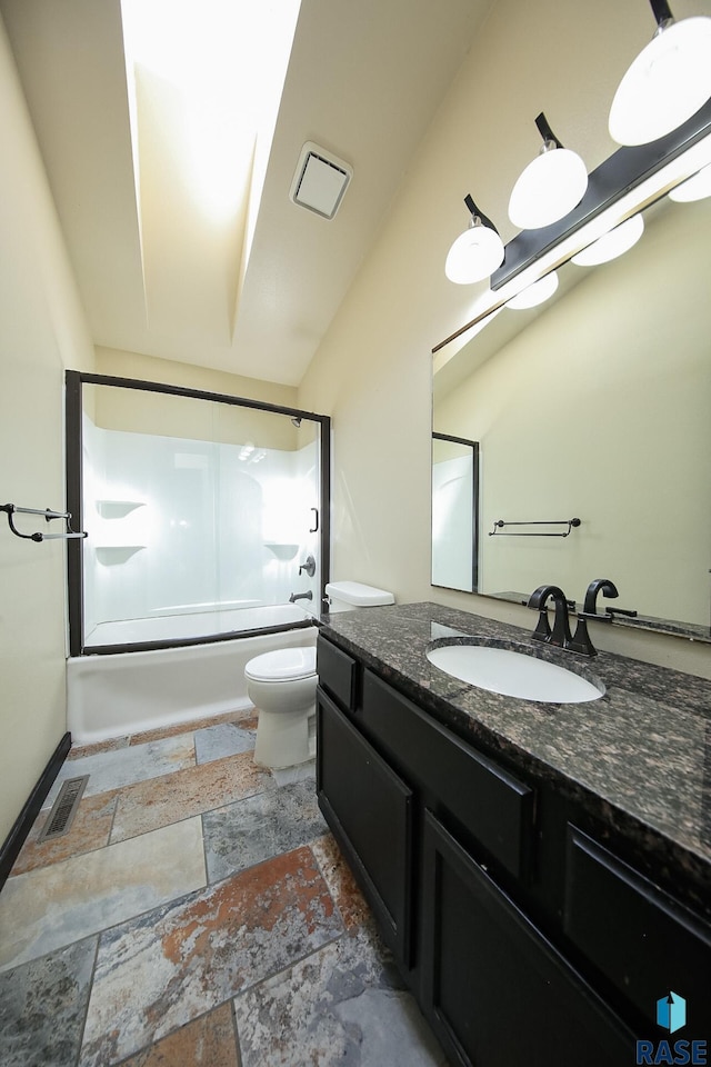 full bath with stone finish floors, toilet, vanity, and shower / bath combination with glass door