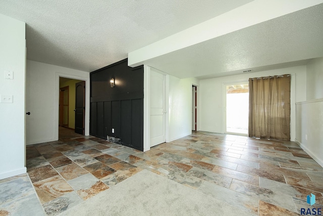 spare room featuring stone tile floors, a textured ceiling, and baseboards
