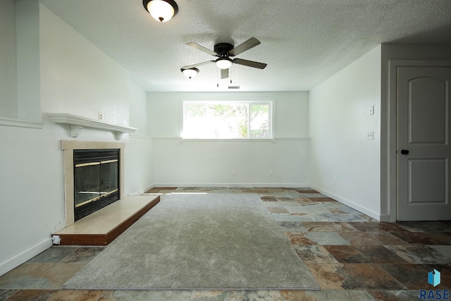 unfurnished living room featuring ceiling fan, baseboards, a glass covered fireplace, stone finish floors, and a textured ceiling