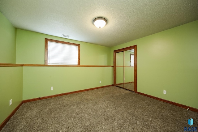 carpeted empty room featuring a textured ceiling and baseboards