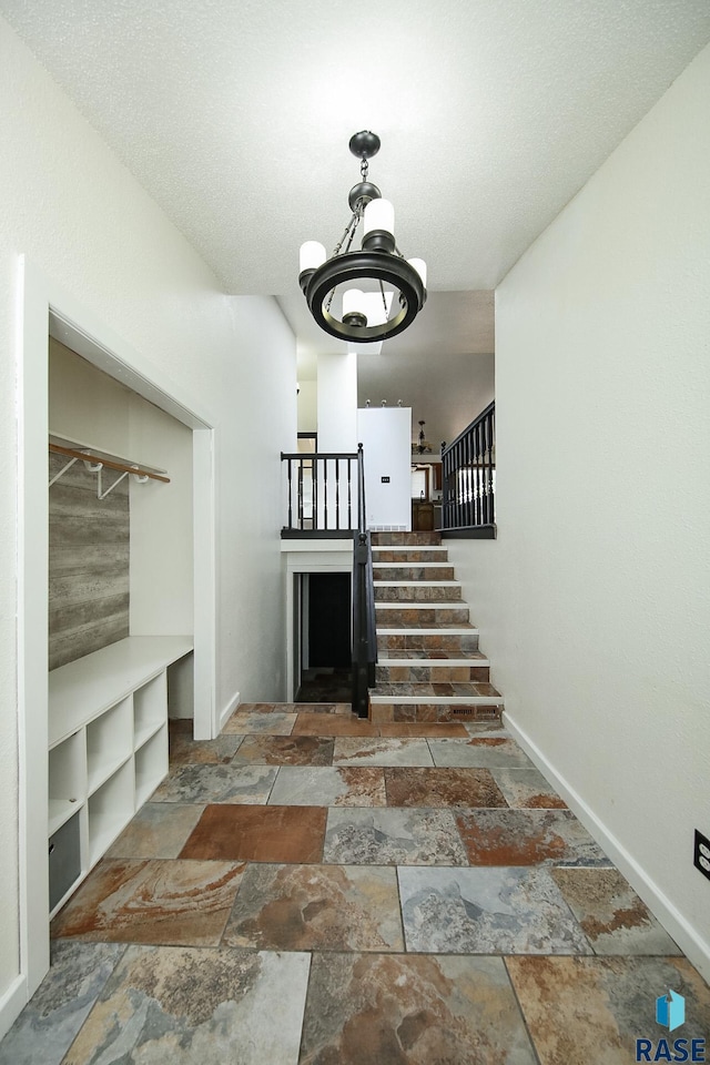 staircase featuring stone tile flooring, a chandelier, and baseboards