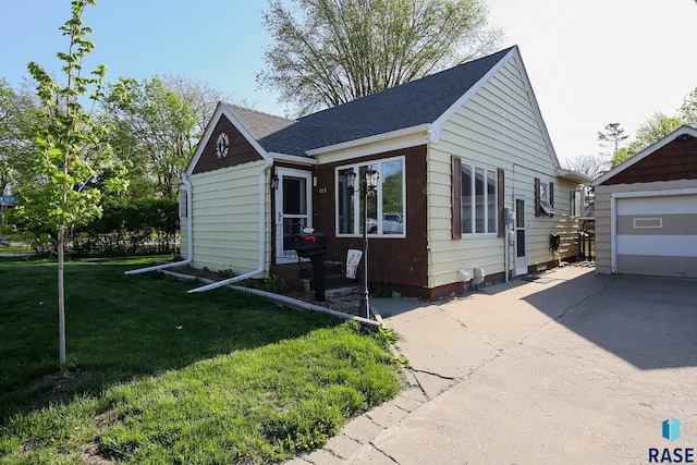 bungalow-style home with an outbuilding, a front lawn, driveway, roof with shingles, and a garage