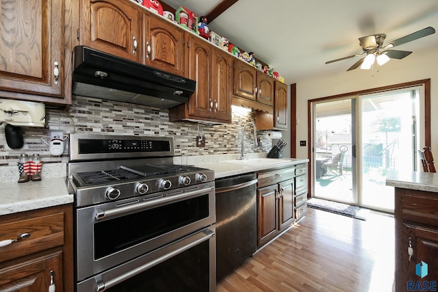 kitchen with appliances with stainless steel finishes, under cabinet range hood, a sink, ceiling fan, and decorative backsplash