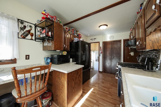 kitchen with exhaust hood, black appliances, a sink, light wood-style floors, and light countertops