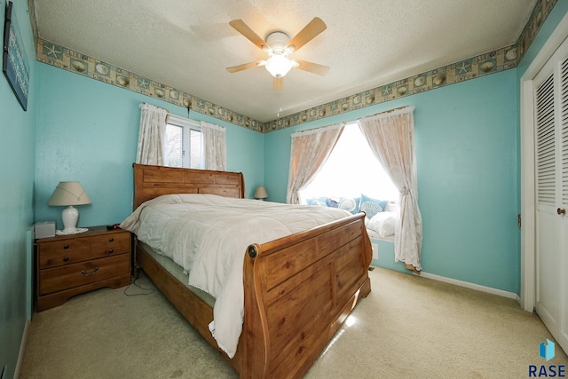 bedroom with a closet, light carpet, a textured ceiling, ceiling fan, and baseboards