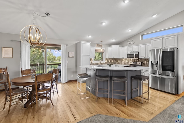 kitchen featuring appliances with stainless steel finishes, vaulted ceiling, a center island, white cabinets, and a chandelier