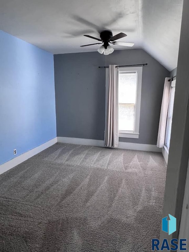 carpeted empty room with ceiling fan, vaulted ceiling, and baseboards