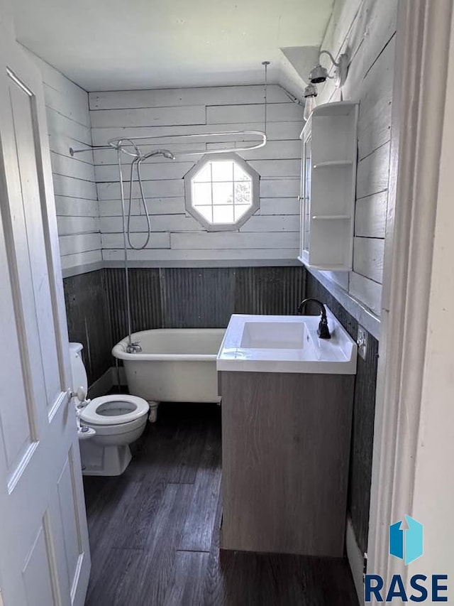 full bath featuring wood finished floors, toilet, wooden walls, vanity, and a bath