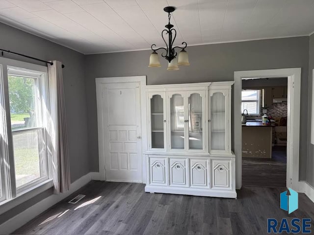 unfurnished dining area with a chandelier, healthy amount of natural light, dark wood-type flooring, and crown molding